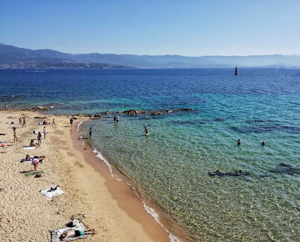 people sunbathing on a beach with blue sea and rocks
